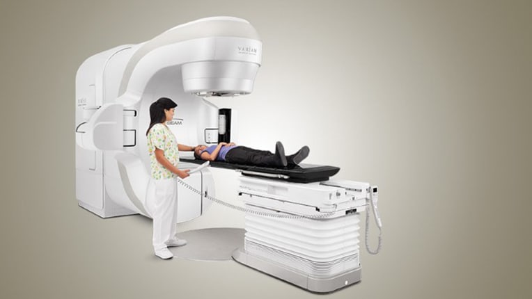 A radiation therapy treatment machine with a clinician positioning a patient on the treatment table
